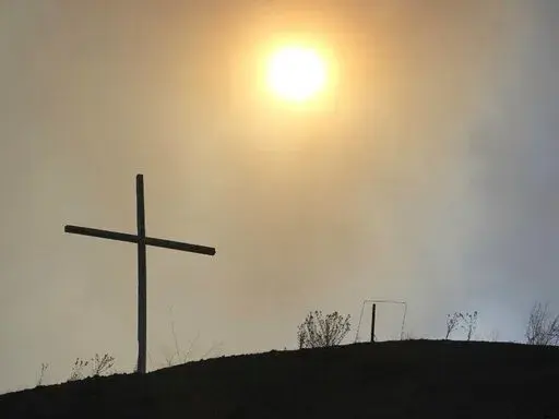 This May 4, 2022 image courtesy of Laura Paskus shows the silhouette of a cross amid smokey skies where hundreds of firefighters are battling a massive wildfire burning in the Sangre de Cristo Mountains near the community of Las Vegas, New Mexico. (Laura Paskus via AP)