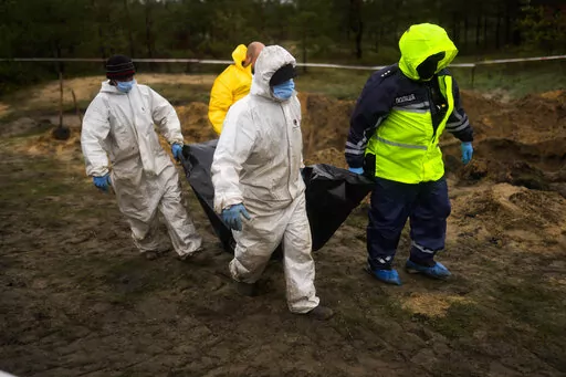 Members of a forensic team carry a plastic bag with a body inside as they work at an exhumation in a mass grave in Lyman, Ukraine, Tuesday, Oct. 11, 2022. (AP Photo/Francisco Seco)