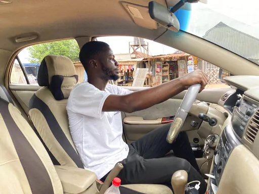 Adenekan Ayomide, 27, an undergraduate student turned a taxi driver following nationwide university strike, poses for a photograph inside his taxi in Abuja, Nigeria, Tuesday, May 10, 2022. “Nobody is talking about school again,” said Ayomide, who said he is now working more than one job and the budget he had for getting through university now looks unrealistic. (AP Photo/Chinedu Asadu)