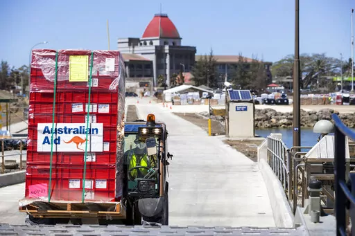 In this photo provided by the Australian Defence Force, la loader is used to move aid supplies at the port at Nuku'alofa, Tonga, Thursday, Jan. 27, 2022, after HMAS Adelaide carried in the disaster relief and humanitarian aid supplies. The danger of spreading the coronavirus was underscored when nearly two dozen sailors aboard the the Adelaide were reported infected on Tuesday, raising fears they could bring the coronavirus to the small Pacific archipelago devastated by an undersea volcanic erup