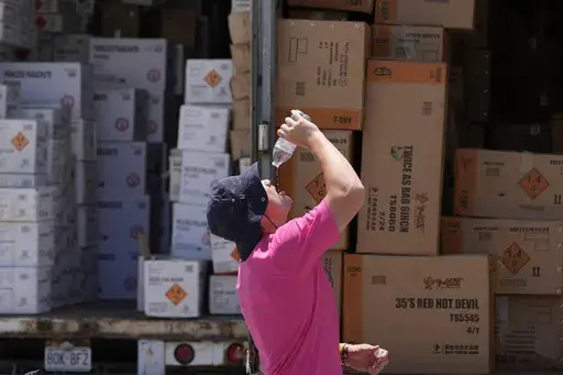 Wyatt Seymore pours the last drops of liquid from a water bottle into his mouth as he takes a break from unloading a stiflingly hot trailer of fireworks outside Powder Monkey Fireworks ahead of the opening of the stand, Monday, June 17, 2024, in Weldon Spring, Mo. (AP Photo/Jeff Roberson)