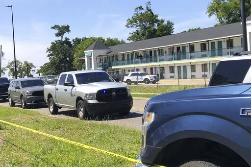 Law enforcement inspect the Biloxi Broadway Inn Express, cordoned off by crime scene tape and vehicles,  in this image provided by WLOX-TV, Wednesday, April 27, 2022.  The fatal shooting at the hotel on Mississippi’s Gulf Coast has police in a standoff with the suspect at a business a few miles away. Gulfport police said the suspect was holed up inside a business Wednesday and officers had shut down access to the area. (Jasmine Lotts/WLOX-TV via AP)