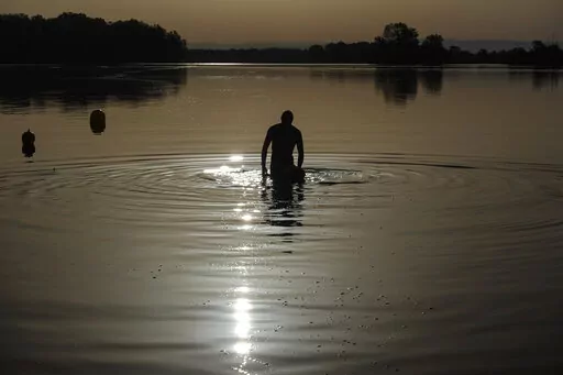 A man walks in the water as the sun rises above the Miribel lake, outside Lyon, central France, Saturday, June 18, 2022. A heat wave that's already lasted more than a week keeps on baking the US, Asia, Europe and even the Arctic. (AP Photo/Laurent Cipriani, File)
