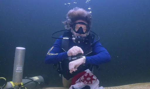 In this photo provided by the Florida Keys News Bureau, diving explorer and medical researcher Dr. Joseph Dituri points to his watch Friday, June 9, 2023, indicating that it is time to surface after spending 100 days in the Jules' Undersea Lodge marine habitat at the bottom of a Key Largo, Fla., lagoon. Dituri broke the previous 73-day record for underwater human habitation at ambient pressure, undertook medical and marine science research and interacted online with more than 5,500 students duri