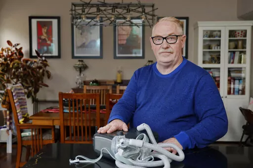 Jeffrey Reed, who experienced persistent sinus infections and two bouts of pneumonia while using a Philips CPAP machine, poses with the device at his home Thursday, Oct. 20, 2022, in Marysville, Ohio. The device is part of a massive global recall of breathing machines triggered by sound-dampening foam that can break down, releasing potentially harmful particles and chemicals. (AP Photo/Jay LaPrete)