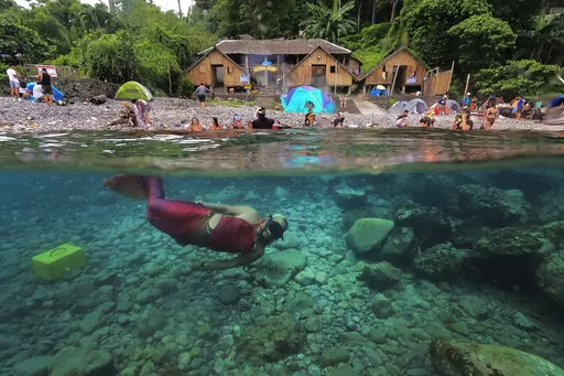 Queen Pangke Tabora swims in her mermaid suit as she conducts a mermaiding class in front of the Ocean Camp in Mabini, Batangas province, Philippines on Sunday, May 22, 2022. For the transgender Filipina woman approaching middle age, seeing her legs encased in vibrant, scaly-looking neoprene three years ago was the realization of a childhood dream. (AP Photo/Aaron Favila)