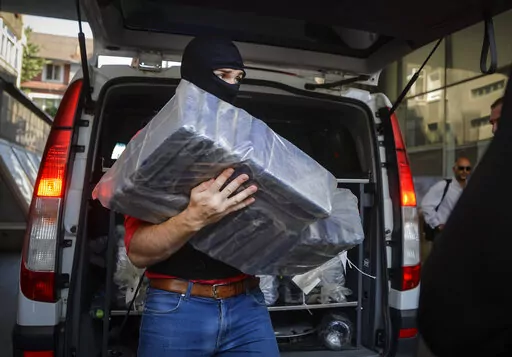 A masked policeman carries packs of cocaine, at the organized crime prosecutor' office in Bucharest, Romania, on July 1, 2016. Records amounts of cocaine are being seized in Europe while manufacturing of the banned stimulant drug is now taking place inside the the European Union, officials in charge of fighting and monitoring drugs use in the bloc warned on Friday, May 6, 2022. (AP Photo/Andreea Alexandru)