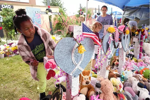 London M., of Allen, Texas, whose mother asked to only use her initial for her last name, signs a cross after signing all the others at a makeshift memorial by the mall where several people were killed, Wednesday, May 10, 2023, in Allen, Texas. (AP Photo/Tony Gutierrez)