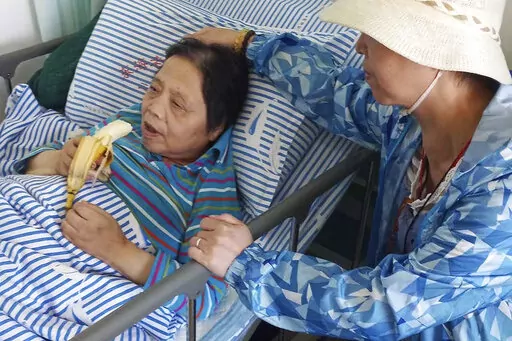 In this photo released by the family of Shen Peiming, Shen Peiming, 71, eats a banana as a family member attends to her at her bed side at the Shanghai Donghai Elderly Care hospital on Sept. 24, 2019.  Shen died  Sunday morning, April 3, 2022, at the hospital, without her loved ones by her side. Her family, unable to visit because of pandemic restrictions, is unsure of the circumstances of her death. The hospital had reported a COVID-19 outbreak, but Shen had tested negative, as of last week. (F