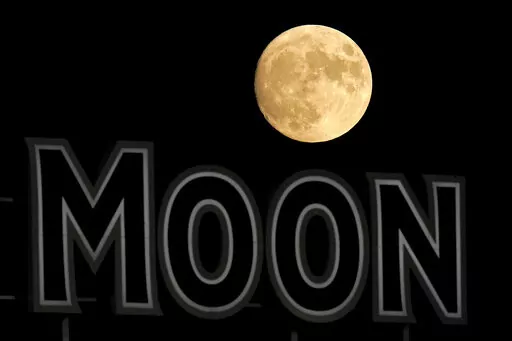 The moon rises beyond a sign in the outfield during the fifth inning of a baseball game between the Kansas City Royals and the Chicago White Sox Wednesday, Aug. 10, 2022, in Kansas City, Mo. With more lunar missions than ever on the horizon, the European Space Agency wants to give the moon its own time zone. In February 2023, the agency said space organizations around the world are considering how best to keep time on the moon. (AP Photo/Charlie Riedel, File)