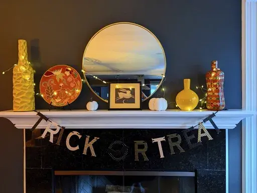 This photo provided by Kim Cook shows her Halloween mantelscape with trick or treat banner, fabric pumpkins, and a color scheme of objects to fit the season. (Kim Cook via AP)