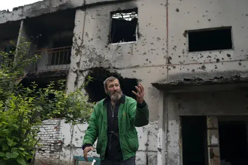 Viacheslav Myronenko, 71, stands in front of the entrance of a damaged building where he lives in the freed village of Hrakove, Ukraine, Tuesday, Sept. 13, 2022. Myronenko has been living in the basement of his bombed-out apartment building with three neighbors for more than four months. (AP Photo/Leo Correa)
