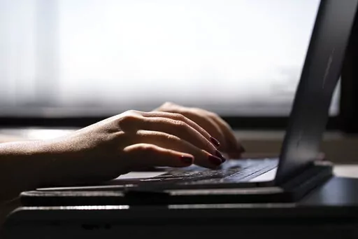 This May 18, 2021, photo shows a woman typing on a laptop on a train in New Jersey.  A movement is growing to shorten the workweek, but trade-offs and barriers should be considered.  (AP Photo/Jenny Kane, File)