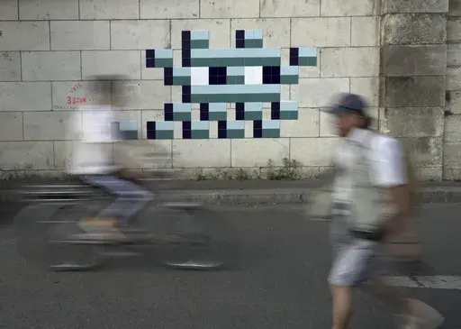 A cyclist rides in front of an Olympic-themed new mosaic by the mysterious French street artist known only by the name Invader, Wednesday Aug. 7, 2024, on the banks of the Seine River, during the 2004 Summer Olympics, in Paris, France. (AP Photo/John Leicester)