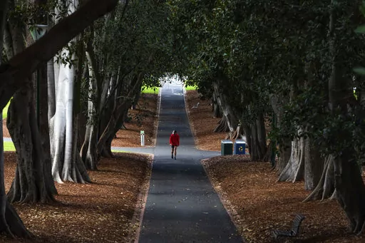 A man wearing a mask is seen walking in a Melbourne park as Melbourne goes into Stage 4 Lockdown due to the spread of COVID-19, Wednesday, Aug. 5, 2020. The coronavirus variant has swept across Australia despite its high vaccination rate and strict border policies that kept the country largely sealed off from the world for almost two years. (AP Photo/Asanka Brendon Ratnayake, File)
