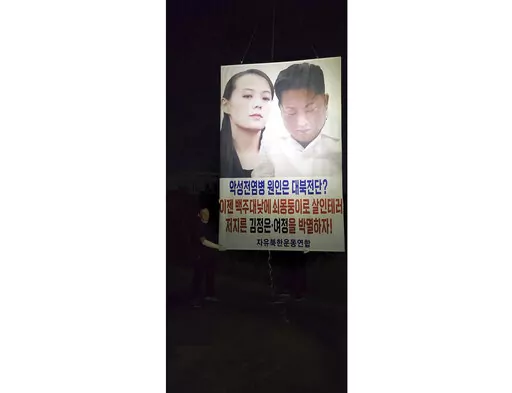 In this photo provided by Fighters for a Free North Korea, Park Sang-hak holds a placard carrying pictures of North Korean leader Kim Jong Un and his sister Kim Yo Jong in Ganghwa, South Korea Sunday, Sept. 4, 2022. Park said he has again flown huge balloons carrying COVID-19 relief items and an anti-North Korea placard across the tense inter-Korean border, despite the North’s recent warning of a deadly attack over his activities. A part of letters read "Let's eradicate Kim Jong Un and (his si