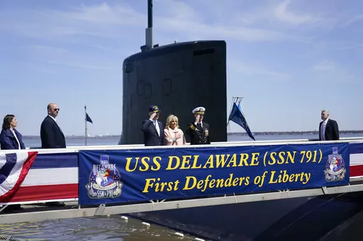 President Joe Biden returns a salute as he stands with first lady Jill Biden and Cmdr. Matthew Horton, Commanding Officer, USS Delaware, before they board the USS Delaware, Virginia-class fast-attack submarine, for a tour at the Port of Wilmington in Wilmington, Del., Saturday, April 2, 2022. (AP Photo/Carolyn Kaster)