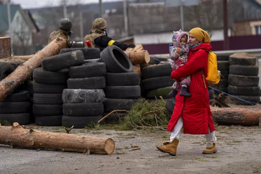 A Ukrainian woman holding a baby walks past a barricade controlled by Ukrainian soldiers as they flee crossing the Irpin river in the outskirts of Kyiv, Ukraine, Saturday, March 5, 2022. (AP Photo/Emilio Morenatti)