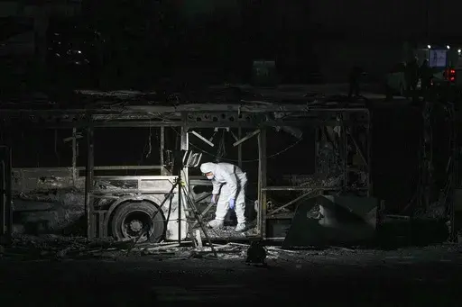 An Israeli police officer inspects the scene of one of a series of bus explosions in what authorities said appeared to be a militant attack in Bat Yam, central Israel, Thursday, Feb. 20, 2025. (AP Photo/Ohad Zwigenberg)