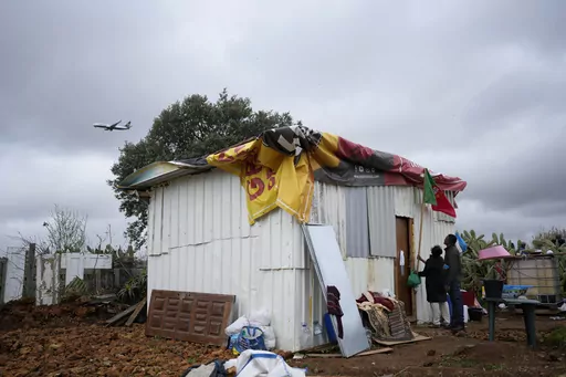 FILE Daisy and a friend attach a Portuguese flag to her makeshift house while a low-cost airline jet approaches for landing in Lisbon, in Loures, Portugal, Monday, March 6, 2023. Daisy was hoping the flag could provide some kind of protection, before the arrival of municipal workers sent to demolish the house. Seven families, mostly immigrants from Sao Tome & Principe, were evicted and had their illegal houses demolished. They had built their houses in the last couple of years when unable to pay