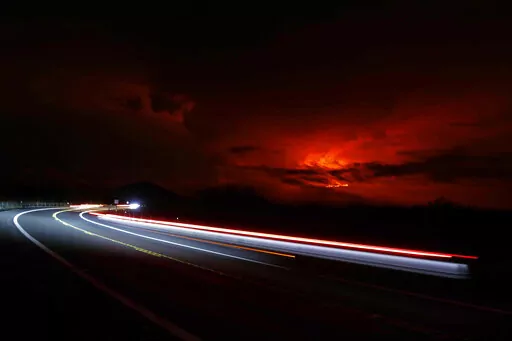 In this long camera exposure, cars drive down Saddle Road as Mauna Loa erupts in the distance, Monday, Nov. 28, 2022, near Hilo, Hawaii. Mauna Loa, the world's largest active volcano erupted Monday for the first time in 38 years. (AP Photo/Marco Garcia)