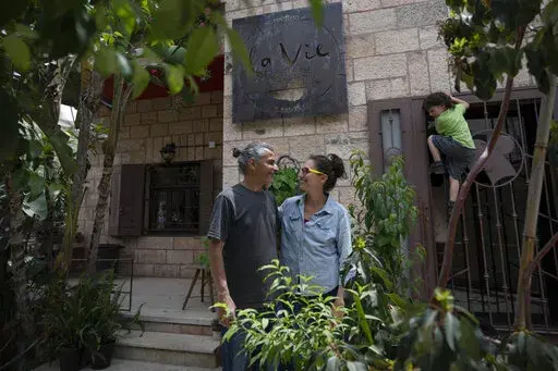 Kenae Totah, 5, right, plays while his parents Morgan Cooper, 41, center and Saleh Totah, right, pose for a photo in front of their restaurant, at the West Bank city of Ramallah, Monday, May 2, 2022.  The Israeli military body in charge of civilian affairs in the occupied West Bank has developed a new policy that would heavily regulate entry into the territory. Critics say it extends Israel's nearly 55-year military rule even further into every corner of Palestinian society. It would impose new 