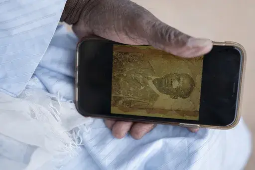 Biram Senghor, whose father was killed in 1944, holds a phone with a photo of his father, in Rufisque, Senegal, Thursday, Nov. 28, 2024. (AP Photo/Sylvain Cherkaoui)