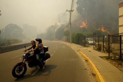 Residents evacuate on a motorcycle amid wildfires into Vina del Mar, Chile, Feb. 3, 2024. Scientists say climate change creates conditions that make the drought and wildfires now hitting South America more likely. (AP Photo/Esteban Felix, File)