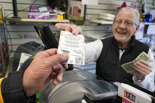 Dot Skoko, owner of Dot's Dollar More or Less shop in Mt. Lebanon, Pa., hands a customer a Mega Millions lottery ticket, Thursday, Jan. 5, 2022. The Mega Millions jackpot has reached an astounding $977 million for Friday night’s drawing after no tickets matched all six numbers drawn on Tuesday night. (AP Photo/Gene J. Puskar, File)