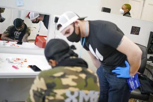 Brian Hackel, right, an overdose prevention specialist, helps Steven Baez, a client suffering addiction, find a vein to inject intravenous drugs at an overdose prevention center, at OnPoint NYC in New York, N.Y., Friday, Feb. 18, 2022.  Also known as a safe injection site, the privately run center is equipped and staffed to reverse overdoses, a bold and controversial contested response to confront opioid overdose deaths nationwide.  (AP Photo/Seth Wenig)