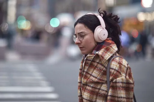 A woman walks using her headphones on Tuesday, Jan. 17, 2023, in New York. After the relative quiet of the pandemic, New York City has come roaring back. Just listen: Jackhammers disrupt the peace and fleets of honking cars, trucks and buses again clog thoroughfares as millions of denizens return to the streets — their voices and clacking heels adding to the ear-splitting din. In one of the world's noisiest cities, the cacophony has returned louder than ever. (AP Photo/Andres Kudacki)
