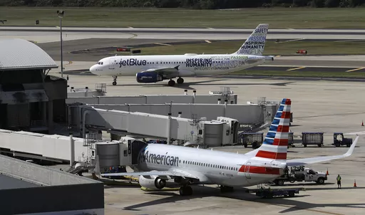 A JetBlue Airbus A320 taxis to a gate on Oct. 26, 2016, after landing, as an American Airlines jet is seen parked at its gate at Tampa International Airport in Tampa, Fla. The two airlines must abandon their partnership in the northeast United States, a federal judge in Boston ruled Friday, May 19, 2023, saying that the government proved that the deal reduces competition in the airline industry. (AP Photo/Chris O'Meara, File)