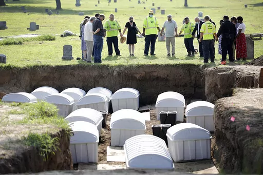 In this July 30, 2021 photo, a group prays during a small ceremony as remains from a mass grave are reinterred at Oaklawn Cemetery in Tulsa, Okla. People who believe they are descendants of Tulsa Race Massacre victims can now provide genetic material to help scientists try to identify remains of possible victims. The committee overseeing the search for mass graves of victims was told Tuesday, June 21, 2022, that enough usable DNA for testing has been found in two of the 14 sets of remains that w