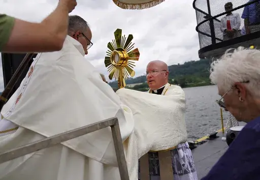Bishop Edward Lohse, apostolic administrator of the Catholic Diocese of Steubenville, left, hands the Eucharist to the Rev. Roger Landry as they board a boat on the Ohio River as part of the National Eucharistic Pilgrimage, at the Steubenville Marina in Steubenville, Ohio, Sunday, June 23, 2024. (AP Photo/Jessie Wardarski)