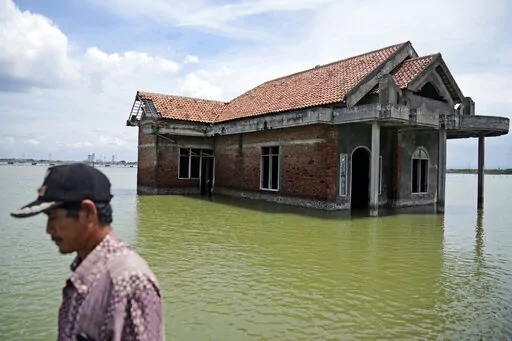 A man walks past a house abandoned after it was inundated by water due to the rising sea level in Sidogemah, Central Java, Indonesia, Nov. 8, 2021. Climate hazards such as flooding, heat waves and drought have worsened more than half of the hundreds of known infectious diseases in people, such as malaria, hantavirus, cholera and even anthrax, according to a new study released Monday, Aug. 8, 2022. (AP Photo/Dita Alangkara, File)
