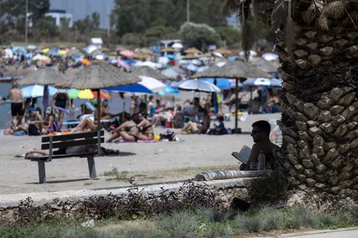 A man reads his book in the shadows of a tree at a beach, at Glyfada suburb, in Athens, Greece, Saturday, July 15, 2023. Greece's Finance Minister promised Wednesday, Aug. 2, 2023, to intensify inspections of beach bars and other businesses renting out seaside chaise lounges and umbrellas, following complaints that non-paying island beachgoers can't find a spot on the sand. (AP Photo/Yorgos Karahalis, File)