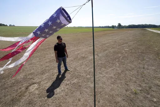 Hay farmer Milan Adams stands in a dry hay field near a wind sock, left, in Exeter, R.I., Tuesday, Aug. 9, 2022. Adams said in prior years it rained in the spring. This year, he said, the dryness started in March, and April was so dry he was nervous about his first cut of hay. (AP Photo/Steven Senne)