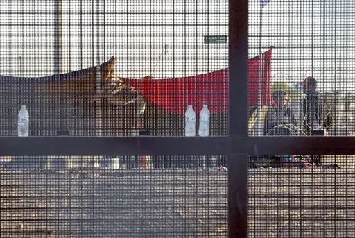 Two migrants, part of a small group, are seeing through the mesh of the border fence as they camp outside a gate in El Paso, Texas, Friday, May 12, 2023. Migrant children in makeshift camps along the U.S.-Mexico border who are waiting to be processed by Border Patrol are in the agency's custody _ something the agency had denied _ and said the Department of Homeland Security must quickly process them and place them in facilities that are “safe and sanitary.”(AP Photo/Andres Leighton, File)