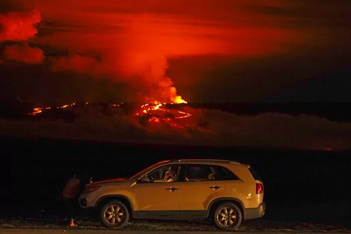 A man talks on a phone in his car alongside Saddle Road as the Mauna Loa volcano erupts Wednesday, Nov. 30, 2022, near Hilo, Hawaii. The world's largest volcano continues to erupt but scientists say lava is no longer feeding the flow front that has been creeping toward a crucial highway. That means the flow isn't advancing and is no longer an imminent threat to the road that connects the east and west sides of the Big Island. (AP Photo/Gregory Bull, File)