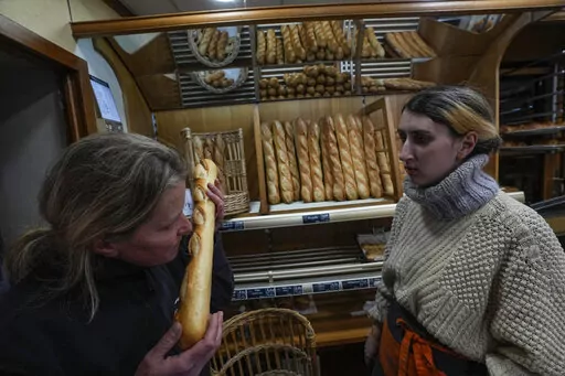 Bakery owner Florence Poirier, LEFT, smells the fresh baguette who comes out of the oven as Mylene Poirier stands next to her at a bakery, in Versailles, west of Paris, Tuesday, Nov. 29, 2022. The humble baguette -- the crunchy ambassador for French baking around the world -- is being added to the U.N.'s list of intangible cultural heritage as a cherished tradition to be preserved by humanity. UNESCO experts gathering Wednesday Nov. 30, 2022 in Morocco decided that the simple French flute deserv