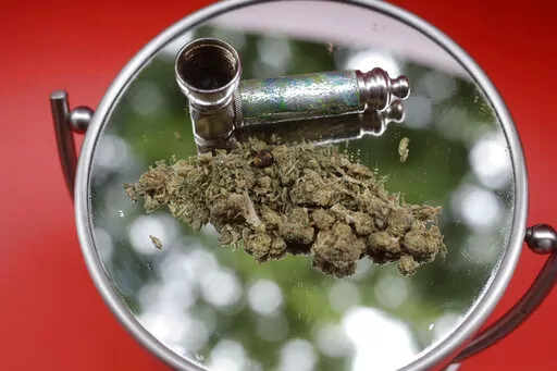 Marijuana and a pipe used to smoke it are displayed on a mirror in New York on June 20, 2018. While New York works on launching a legal market for recreational marijuana, some entrepreneurs have jumped into a legal gray area by saying they're not selling pot but giving it away while people buy something else. (AP Photo/Peter Morgan, File)