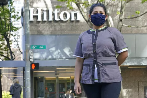Sonia Guevara poses for a photo, Wednesday, May 18, 2022, outside the Hilton hotel where she works as a housekeeper in downtown Seattle. Many hotels across the United States have done away with daily housekeeping service, making what was already one of the toughest jobs in the hospitality industry even more grueling. (AP Photo/Ted S. Warren)