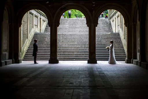 In this Tuesday, May 23, 2017 file photo, a bride and groom pose for wedding pictures at the Bethesda Terrace in New York's Central Park. Industry experts predict 2.5 million weddings in the U.S. this year, a 40-year high. That means millions of invited guests are weighing whether to attend — and how to cover costs if they do.   (AP Photo/Mary Altaffer, file)