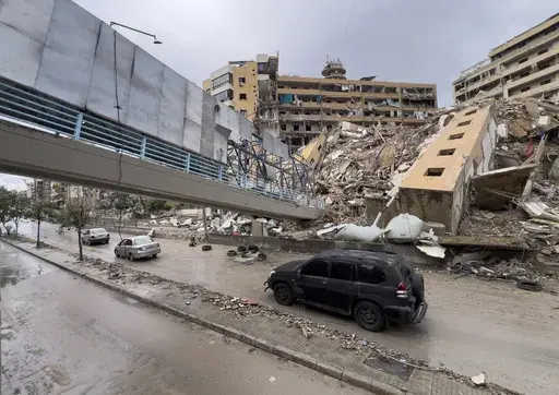 Cars pass under a collapsed pedestrian bridge and next of a destroyed building that were hit in an Israeli airstrike in Dahiyeh, in the southern suburb of Beirut, Lebanon, Tuesday, Nov. 19, 2024. (AP Photo/Hussein Malla)