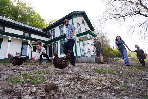 Soraya Holden, left, chases a chicken while walking with her family past their family home, Thursday, May 12, 2022, in Proctor, Vt. After fleeing one of the most destructive fires in California, the Holden family wanted to find a place that had not been so severely affected by climate change and chose Vermont. (AP Photo/Charles Krupa)