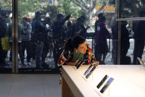 As shoppers wait in the background, a woman looks at Apple's new iPhone 15 at an Apple Store in Los Angeles, Friday, Sept. 22, 2023. On Friday, the Commerce Department issues its August report on consumer spending. (AP Photo/Jae C. Hong, File)