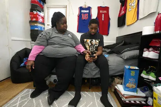 LaTonya Peterson sits with her son Joshua Jackson, 16, as he attends school on his phone at home in Detroit, Friday, Jan. 7, 2022. Like many other parents in the 51,000-student Detroit Public Schools Community District, Peterson is faced once again with juggling home and work schedules around the educational needs of her son. (AP Photo/Paul Sancya)