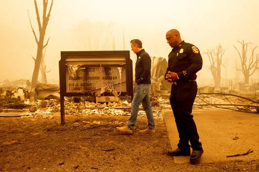 California Gov. Gavin Newsom examines a church marquee while visiting Greenville, which suffered extensive structure loss during the Dixie Fire, on Aug. 7, 2021, in Plumas County, Calif. Accompanying him is Cal Fire Assistant Region Chief Curtis Brown. Democratic governors such as California's Newsom and Washington's Jay Inslee have been clear about their plans to boost spending on climate-related projects, including expanding access to electric vehicles and creating more storage for clean energ