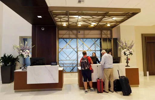 FILE- In this Sept. 5, 2018, file photo guests stand at the front desk at the Embassy Suites by Hilton hotel in Seattle's Pioneer Square neighborhood in Seattle. Many major hotel chains are embracing all-inclusive offerings. For example, Hyatt recently announced an integration with AMR Collection brands, a group of about 100 all-inclusive resorts. Others, including Walt Disney World Resort, are workshopping the all-inclusive model, offering more specialized entertainment or outdoor access. These