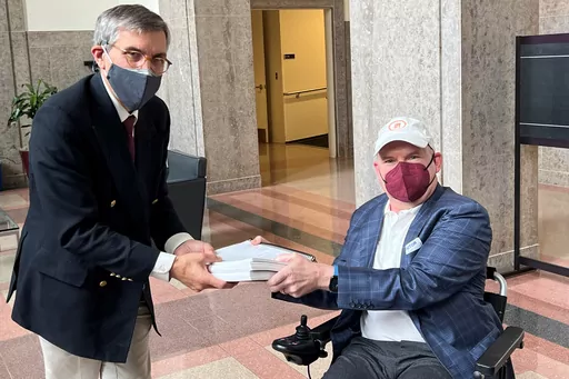 In this photo provided by I AM ALS, Dan Tate, right, delivers a printed petition from ALS patients and advocates to Dr. Peter Marks, left, director of the Food and Drug Administration's center for biologics at the FDA campus in Silver Spring, Md., on Dec. 14, 2022. The FDA meets this week to consider approval of an experimental treatment for Lou Gehrig’s disease, the culmination of a yearslong lobbying effort by patients with the fatal, neurodegenerative disease. Those advocates still face one